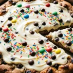 Cookie pizza topped with frosting sprinkles and chocolate candy cut into slices